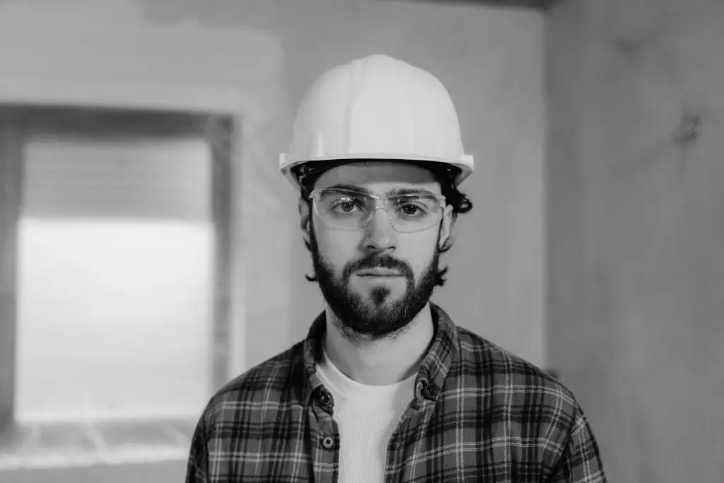 A focused construction worker wearing a hard hat stands indoors, ready for work.